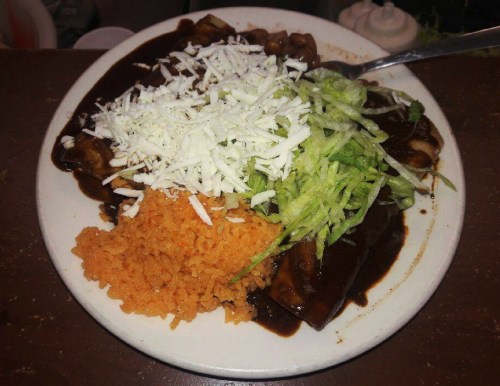 A plate of enchiladas topped with shredded cheese and lettuce, served with a side of orange rice.