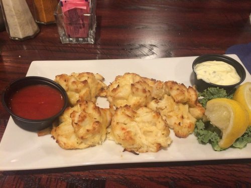 A plate of crab cakes with dipping sauces, garnished with lemon wedges and lettuce.