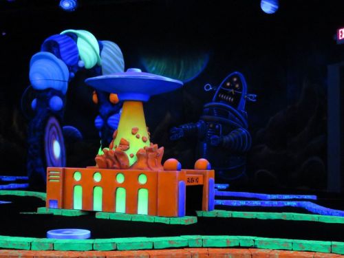 A colorful, glowing miniature scene featuring a UFO, a robot, and a vibrant landscape with planets in the background.