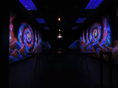 A dimly lit room with vibrant, swirling galaxy murals on the walls and a table in the center.