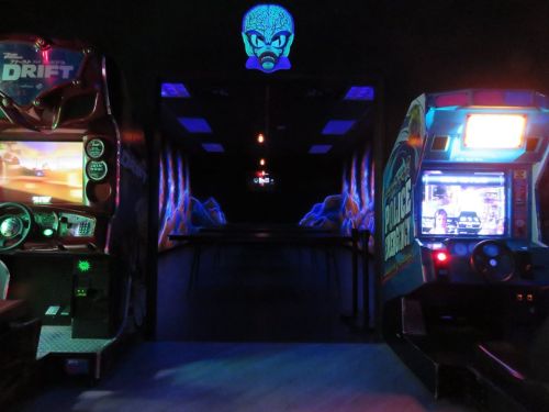 A dimly lit arcade featuring racing games and a glowing mural of a blue octopus on the wall.