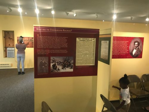 A museum exhibit on the Underground Railroad, featuring informational panels and visitors exploring the space.