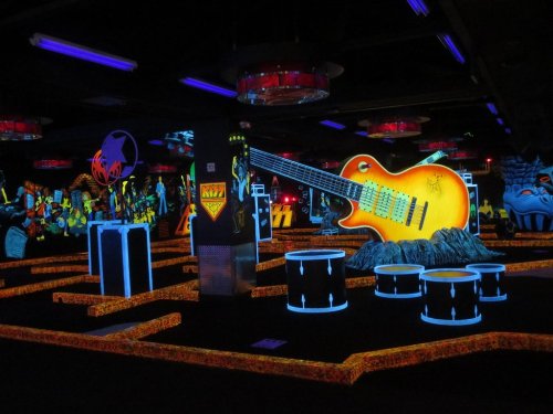 A vibrant glow-in-the-dark mini-golf course featuring oversized musical instruments and colorful decorations.