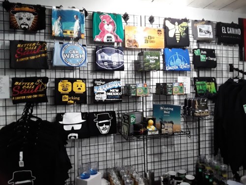 A display of various themed T-shirts and merchandise, including "Breaking Bad" and "Better Call Saul" items on a grid wall.