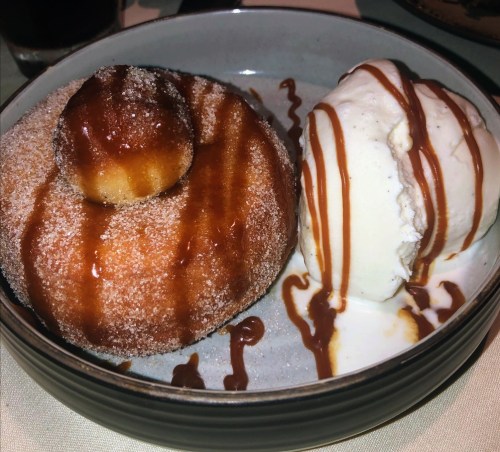 A cinnamon sugar donut drizzled with caramel, served alongside a scoop of vanilla ice cream.