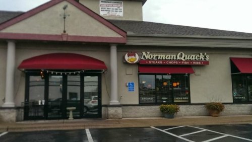 Exterior of NormanQuack's restaurant featuring a sign, red awnings, and large windows on a rainy day.