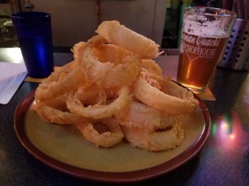 A large pile of golden, crispy onion rings on a plate, with a glass of beer in the background.