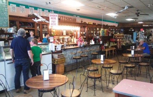 A cozy café interior with a counter, customers ordering, and tables set for dining. Brightly lit and inviting atmosphere.