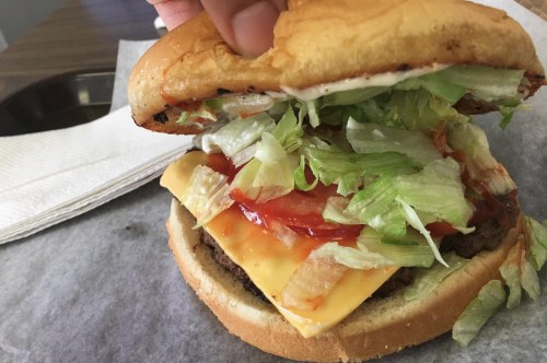 A hand holding a cheeseburger with lettuce, ketchup, and a toasted bun, resting on a paper-lined surface.