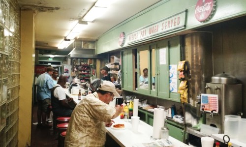 A cozy diner interior with patrons at the counter, enjoying food and drinks in a retro setting.