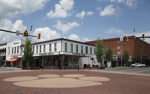 A street view of a corner building with shops, featuring a large paw print design on the pavement and a blue sky.