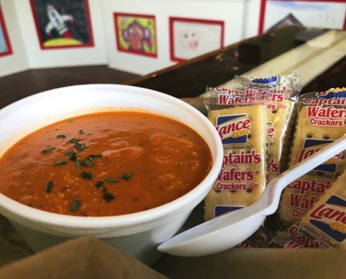 A bowl of tomato soup garnished with herbs, accompanied by crackers on a tray.