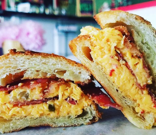 Close-up of a toasted sandwich filled with scrambled eggs, bacon, and cheese, cut in half to show the filling.