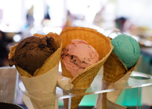 Three ice cream cones with chocolate, strawberry, and blue raspberry flavors displayed in a bright setting.
