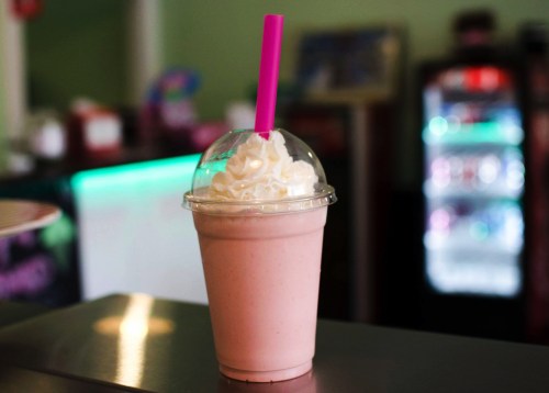 A creamy pink milkshake topped with whipped cream and a pink straw, set against a blurred background.