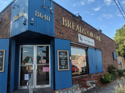 Exterior of "Breads on Oak," a brick building with blue accents, featuring a welcoming entrance and outdoor seating.