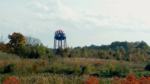 A colorful water tower with a striped red and white top stands amidst a field of autumn foliage and trees.