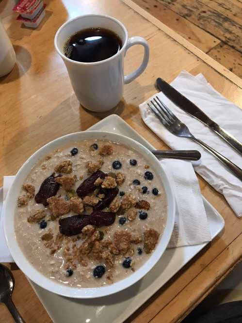 A bowl of oatmeal topped with blueberries and granola, alongside a cup of black coffee on a wooden table.