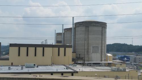 Three large industrial cooling towers and a building under a cloudy sky, with power lines in the foreground.