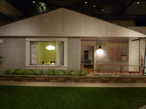A modern house exterior with a large window, green lawn, and decorative plants in front.