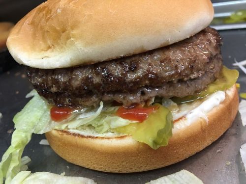 A close-up of a hamburger with a beef patty, lettuce, pickles, ketchup, and mayonnaise on a soft bun.