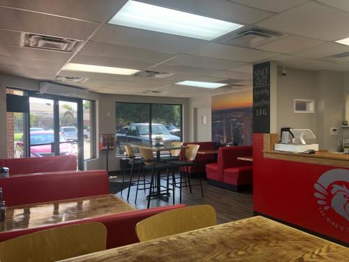 Interior of a casual dining restaurant with red seating, wooden tables, and large windows showing a parking lot outside.