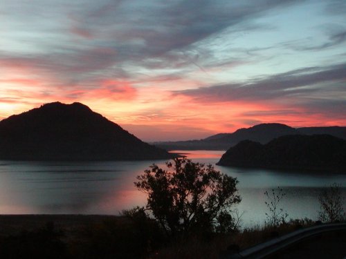 A serene sunset over a lake, with silhouetted mountains and colorful clouds reflecting on the water's surface.