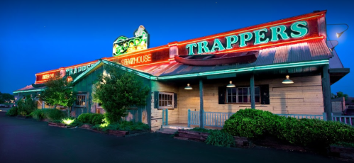 A brightly lit seafood restaurant with neon signs reading "Trappers" against a twilight sky.