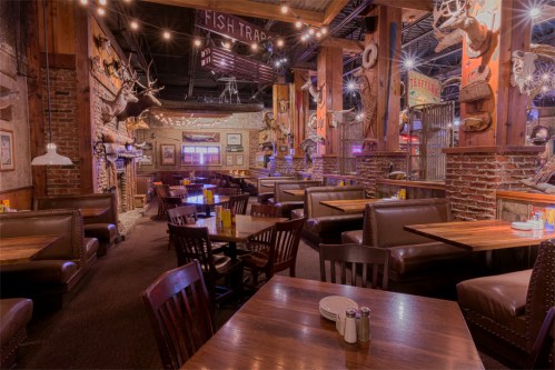 Interior of a rustic restaurant with wooden tables, leather seating, and mounted animal heads on the walls. Warm lighting.