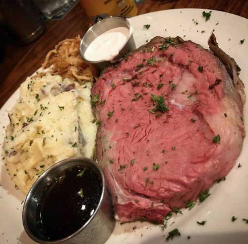 A plate featuring a juicy slice of prime rib, creamy mashed potatoes, crispy onions, and dipping sauce.