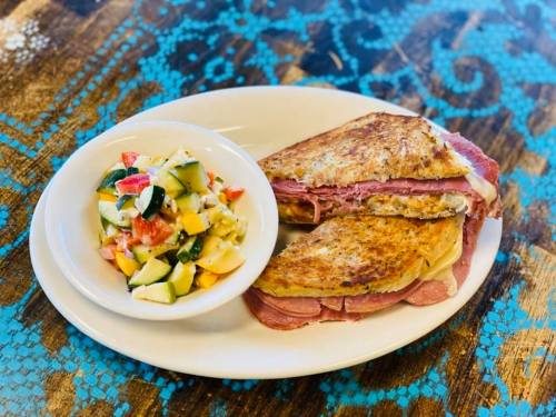 A grilled sandwich with ham and cheese, served with a side of fresh vegetable and fruit salad on a wooden table.
