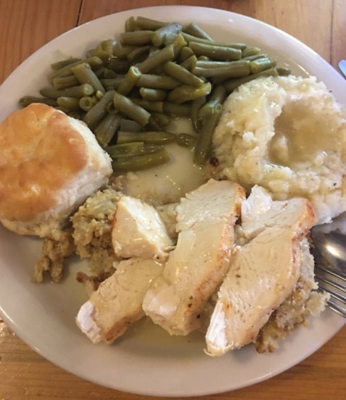 A plate of food featuring sliced chicken, stuffing, green beans, mashed potatoes with gravy, and a biscuit.