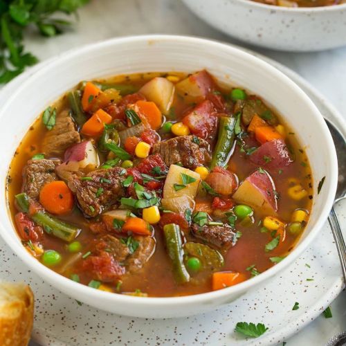 A hearty bowl of beef vegetable soup with carrots, potatoes, corn, and green beans, garnished with fresh herbs.