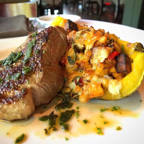 A plate featuring a grilled steak alongside a stuffed acorn squash filled with vegetables and cheese.
