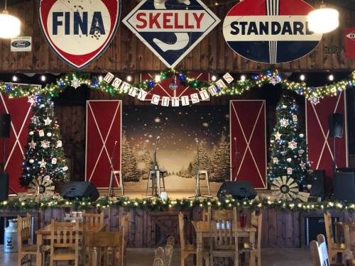 A festive stage decorated with Christmas trees, lights, and signs, set in a rustic wooden venue.