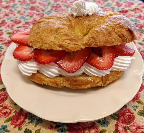 A croissant filled with whipped cream and fresh strawberries, served on a floral-patterned tablecloth.