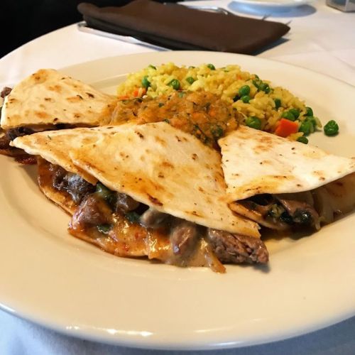 A plate of quesadillas filled with beef, served with rice mixed with peas and carrots, and a side of salsa.