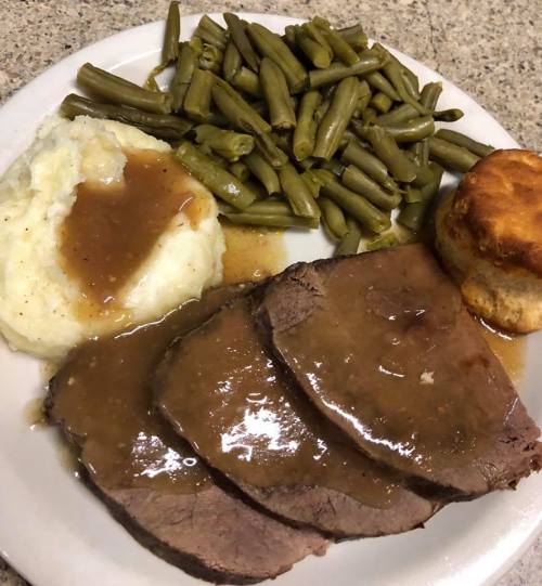 A plate of sliced roast beef with gravy, mashed potatoes, green beans, and a biscuit.