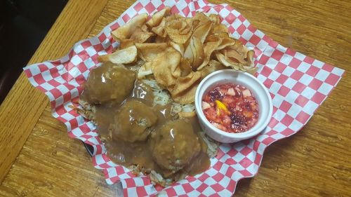 A plate of meatballs with gravy, served over a bed of shredded potatoes, accompanied by crispy chips and a dipping sauce.