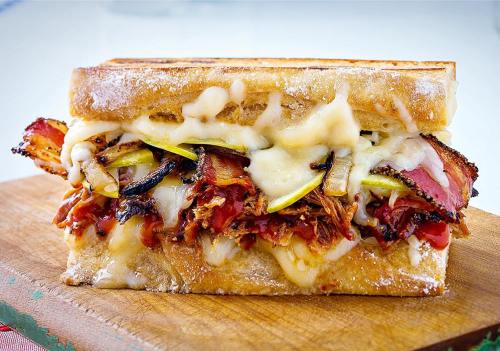 A delicious sandwich filled with pulled pork, melted cheese, and grilled vegetables on toasted bread.