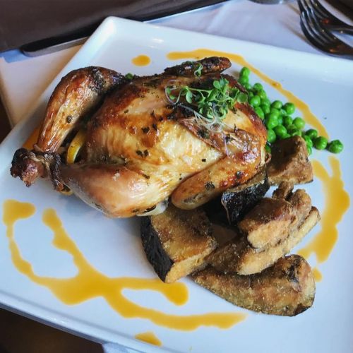 A roasted chicken served with green peas and crispy fried plantains on a white plate, drizzled with sauce.