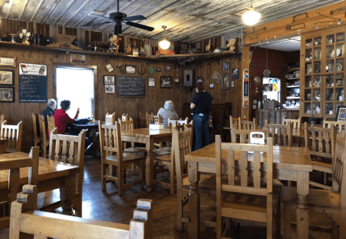 Cozy rustic restaurant interior with wooden tables, chairs, and a few patrons enjoying their meals.