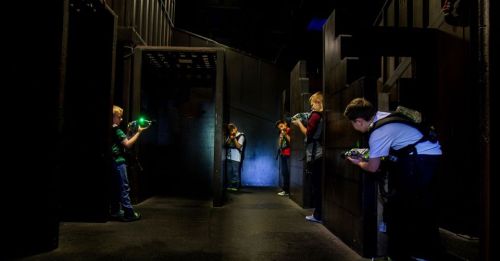 Children playing laser tag in a dark, maze-like arena, aiming their laser guns at targets.