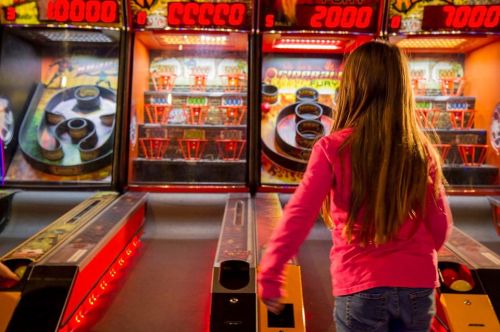 A girl with long hair plays a skee-ball game in an arcade, focused on scoring points.