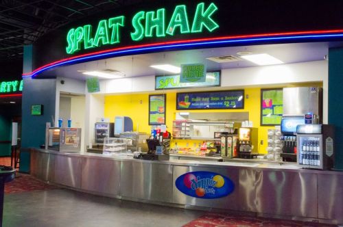 Brightly lit concession stand named "Splat Shak" with colorful signage and various food and drink options.