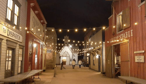 A charming, illuminated street in a historic town at night, with string lights and wooden buildings.