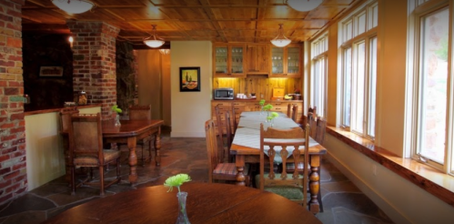 Cozy dining area with wooden tables, chairs, and large windows, featuring rustic decor and a warm atmosphere.