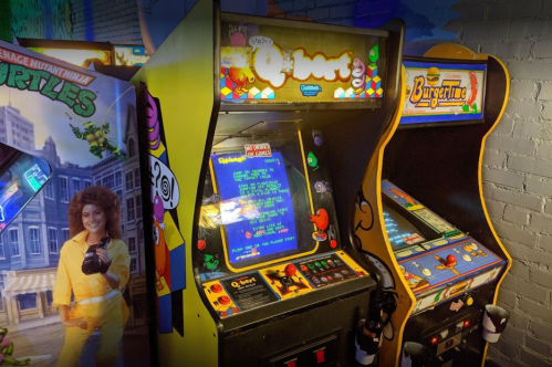 Two vintage arcade machines, "Q*bert" and "BurgerTime," in a colorful gaming environment.