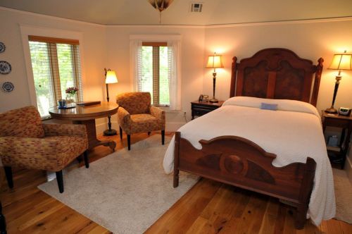 Cozy bedroom with a wooden bed, two chairs, a round table, and large windows letting in natural light.