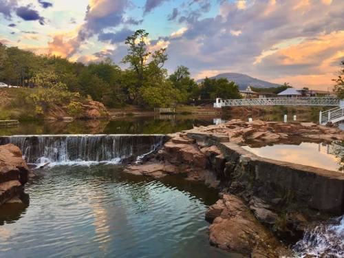 A serene landscape featuring a waterfall cascading into a calm lake, surrounded by trees and a colorful sunset sky.